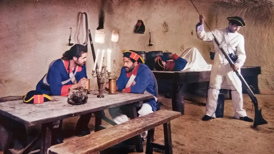 Trois figurants en uniformes du XVIIIe siècle dans une pièce de pierre