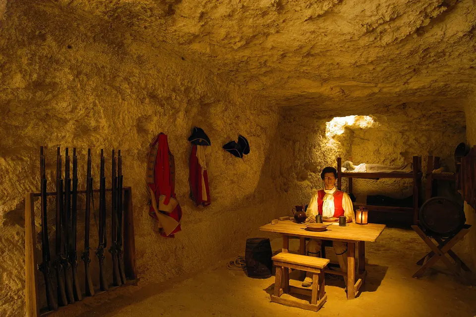 Reconstitution historique dans une pièce creusée dans la roche, avec mobilier et armes