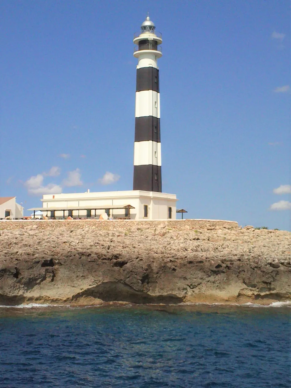 Far amb franges negres i blanques sobre un penya-segat vora el mar
