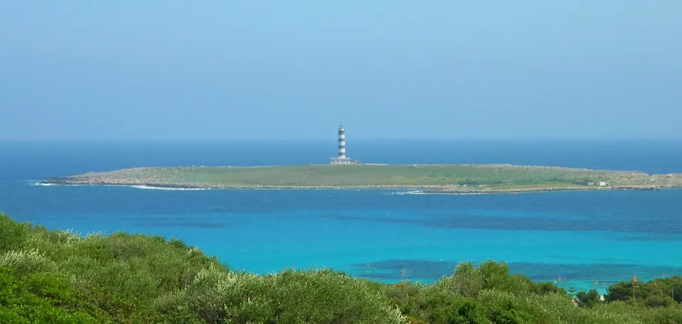 Illa amb un far enmig d’un mar turquesa vista des de la costa