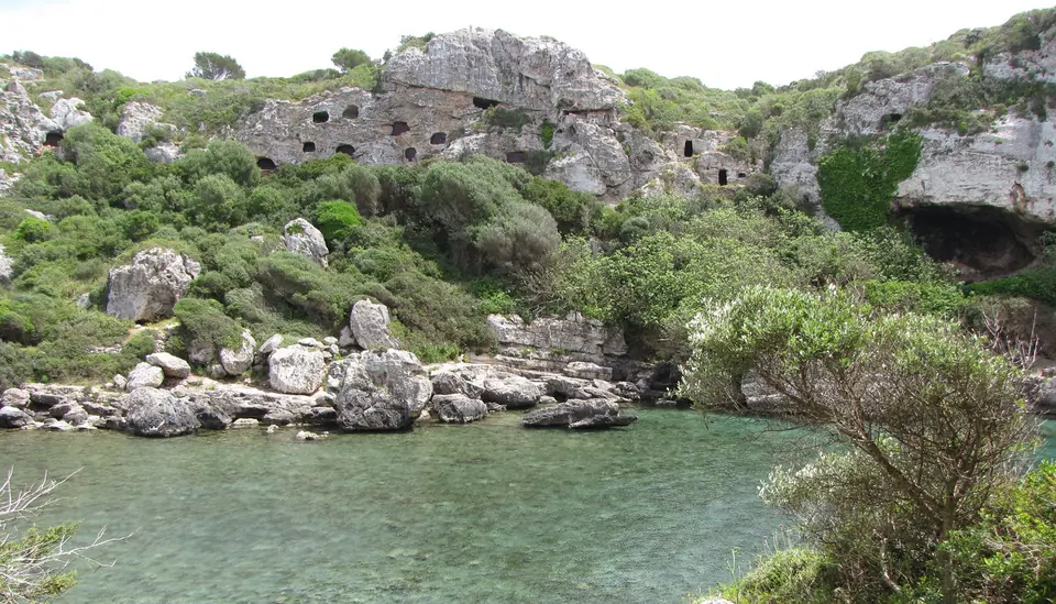 Cala estreta d’aigües tranquil·les amb coves excavades als penya-segats de Cales Coves